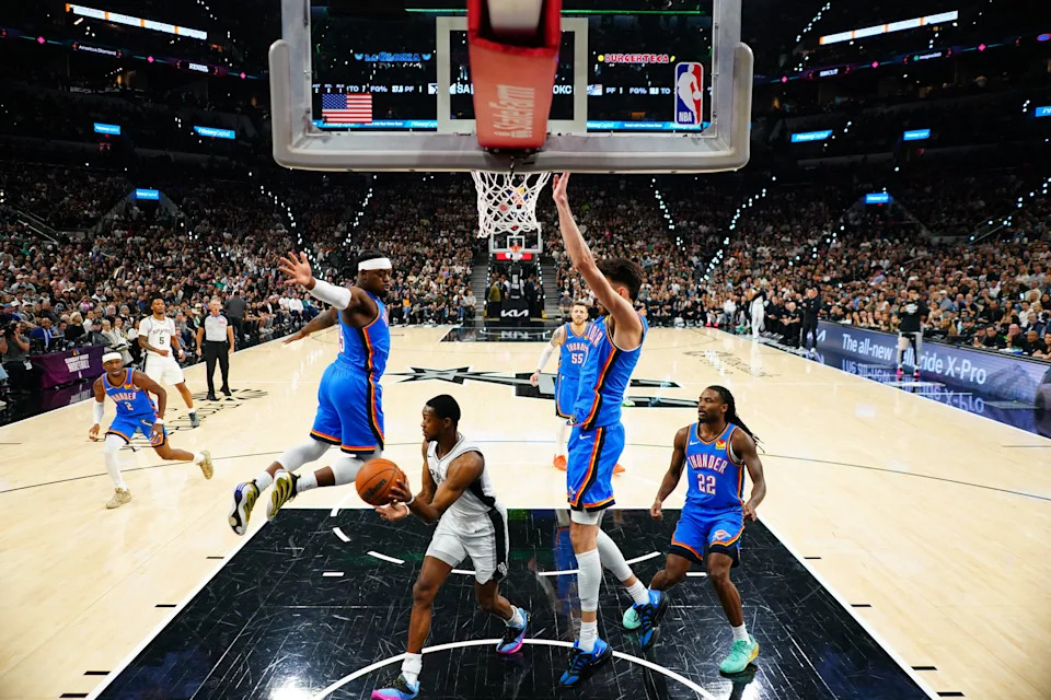May 24, 2026; San Antonio, Texas, USA; San Antonio Spurs guard De'Aaron Fox (4) passes while defended by Oklahoma City Thunder forward Luguentz Dort (5) and center Chet Holmgren (7) in the first half during game four of the western conference finals for the 2026 NBA playoffs at Frost Bank Center. Mandatory Credit: Scott Wachter-Imagn Images