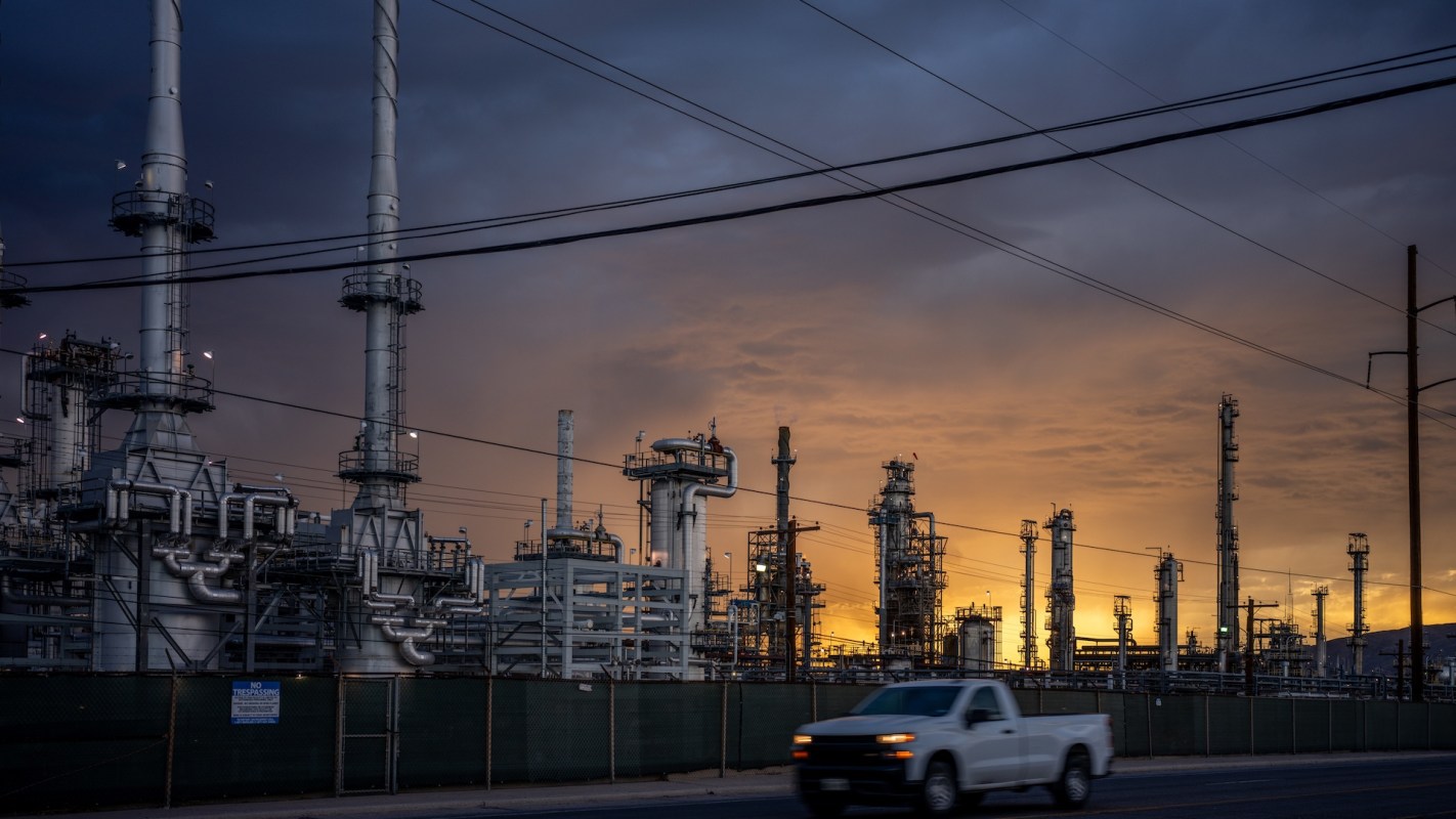 An industrial complex with tall structures and pipes against a sunset sky.