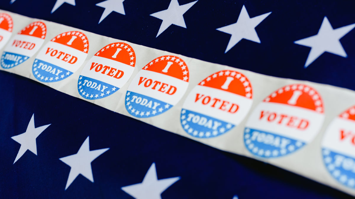 A photographic illustration depicting a strip of I voted stickers over two rows of whites stars over a blue background.