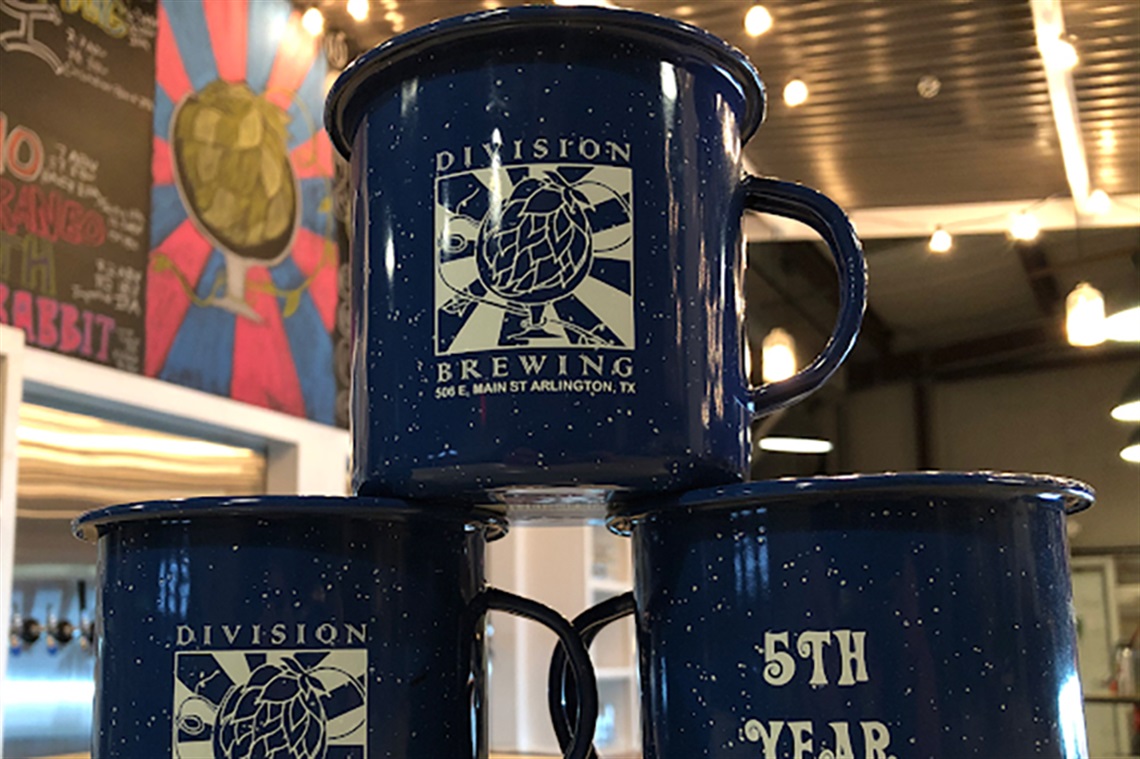 A mug stacked on top of two mugs as its base with the Division Brewing logo and text on the mugs.