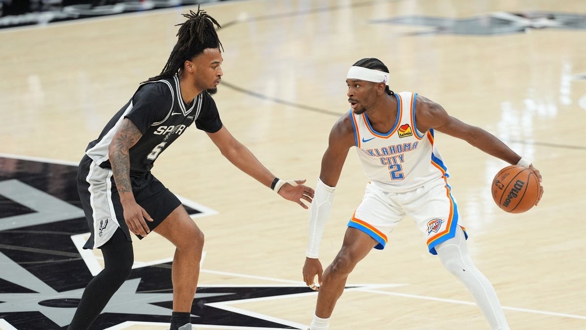 Oklahoma City Thunder guard Shai Gilgeous-Alexander dribbling basketball against San Antonio Spurs guard Stephon Castle