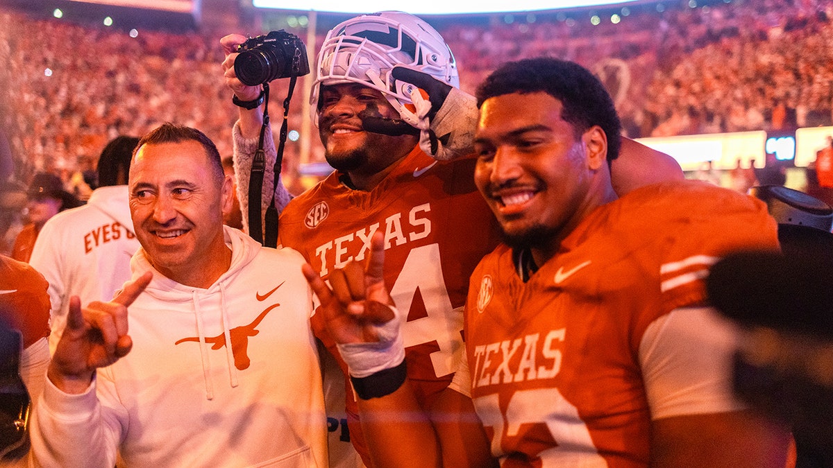 Texas head coach Steve Sarkisian celebrating with offensive linemen Trevor Goosby and Brandon Baker on the field