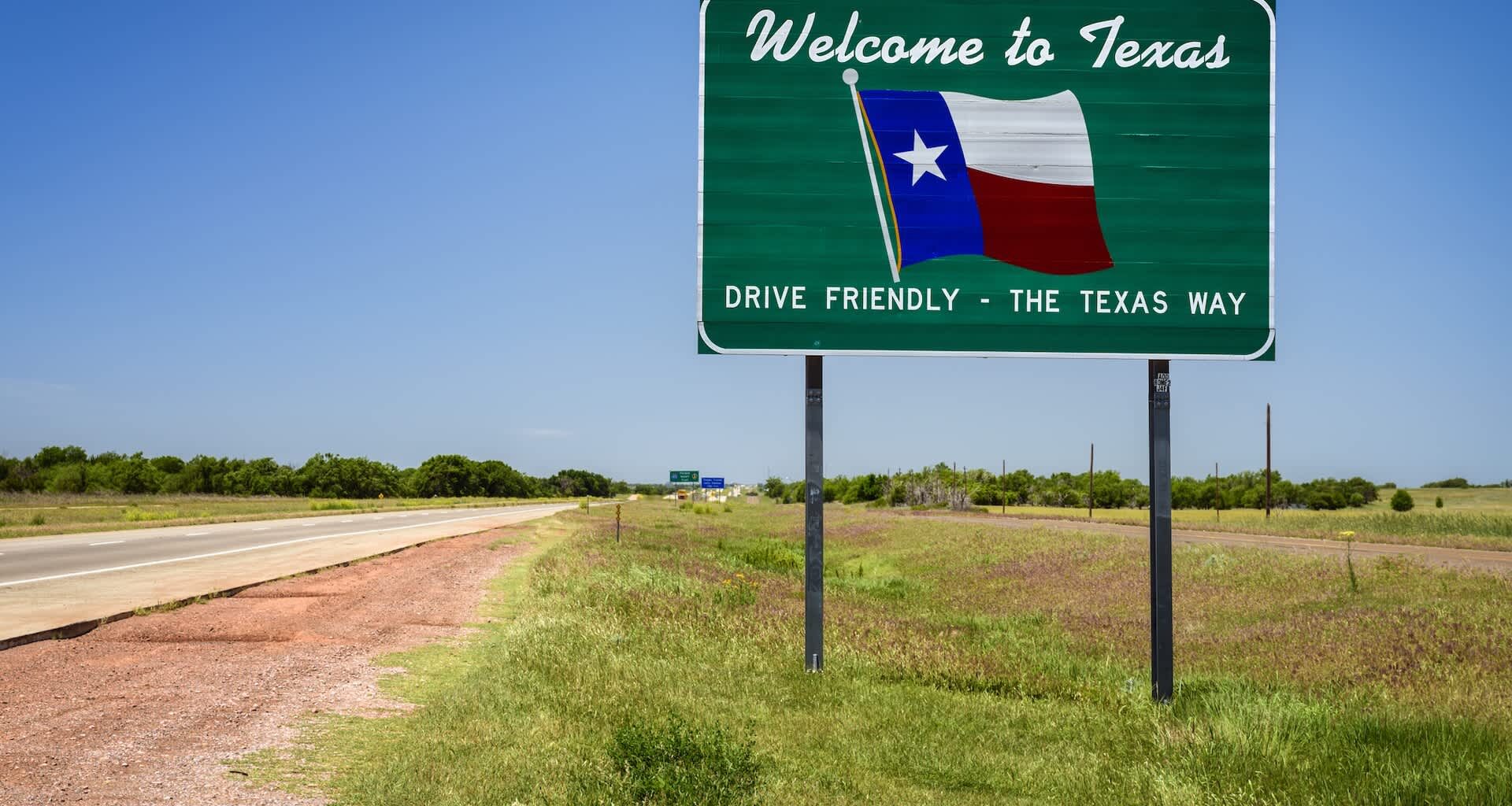 A "Welcome to Texas" sign along a road under a blue sky.