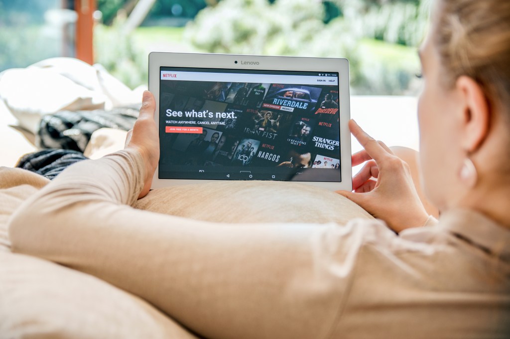 Woman launches Netflix application on Lenovo tablet, displaying various TV show titles.