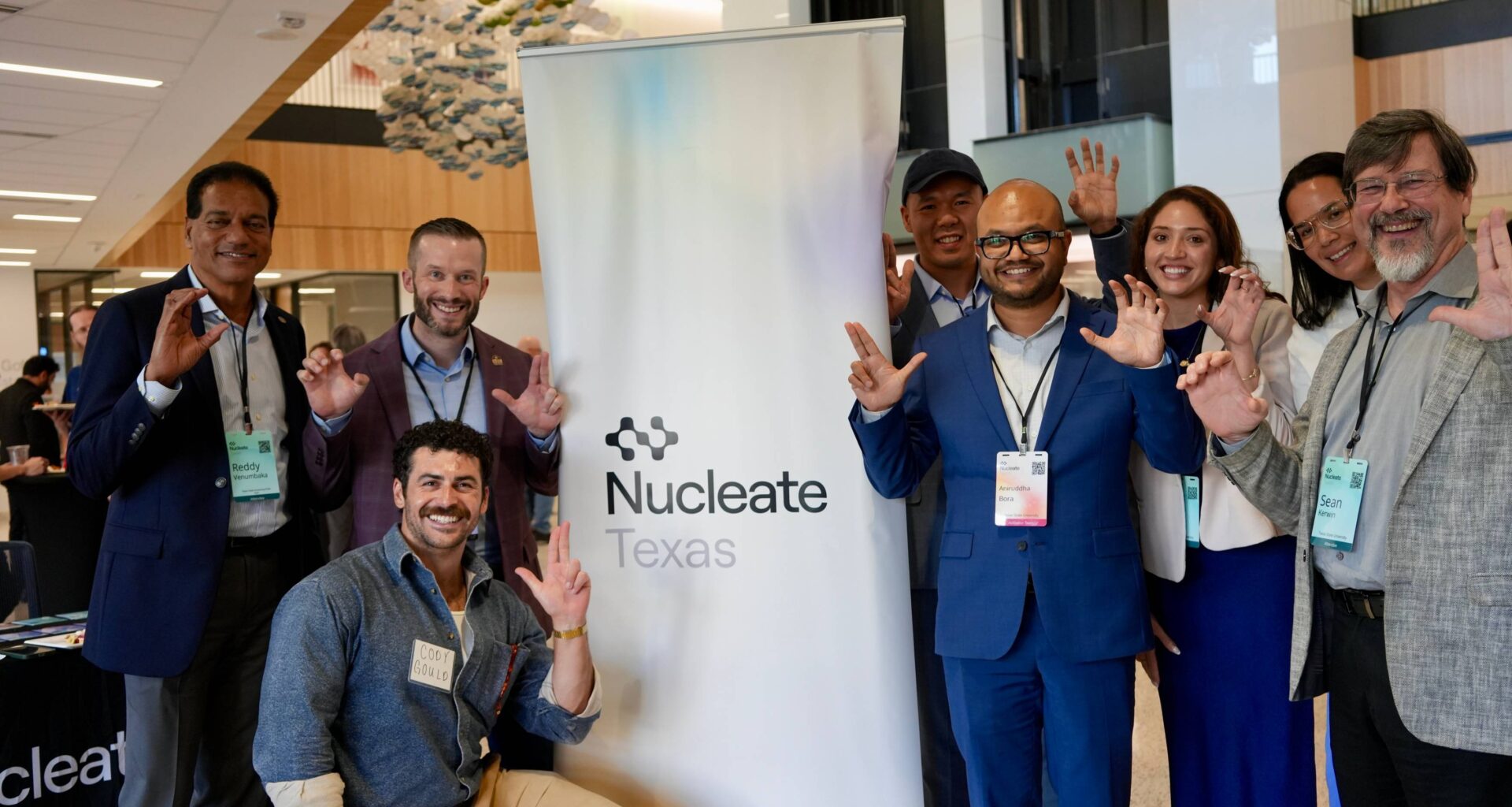 large group of people holding up txst hand signs around sign that reads "nucleate"