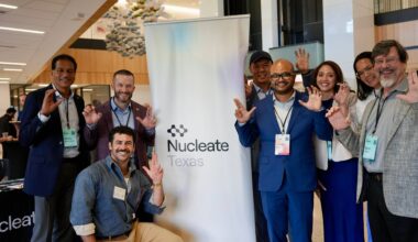 large group of people holding up txst hand signs around sign that reads "nucleate"