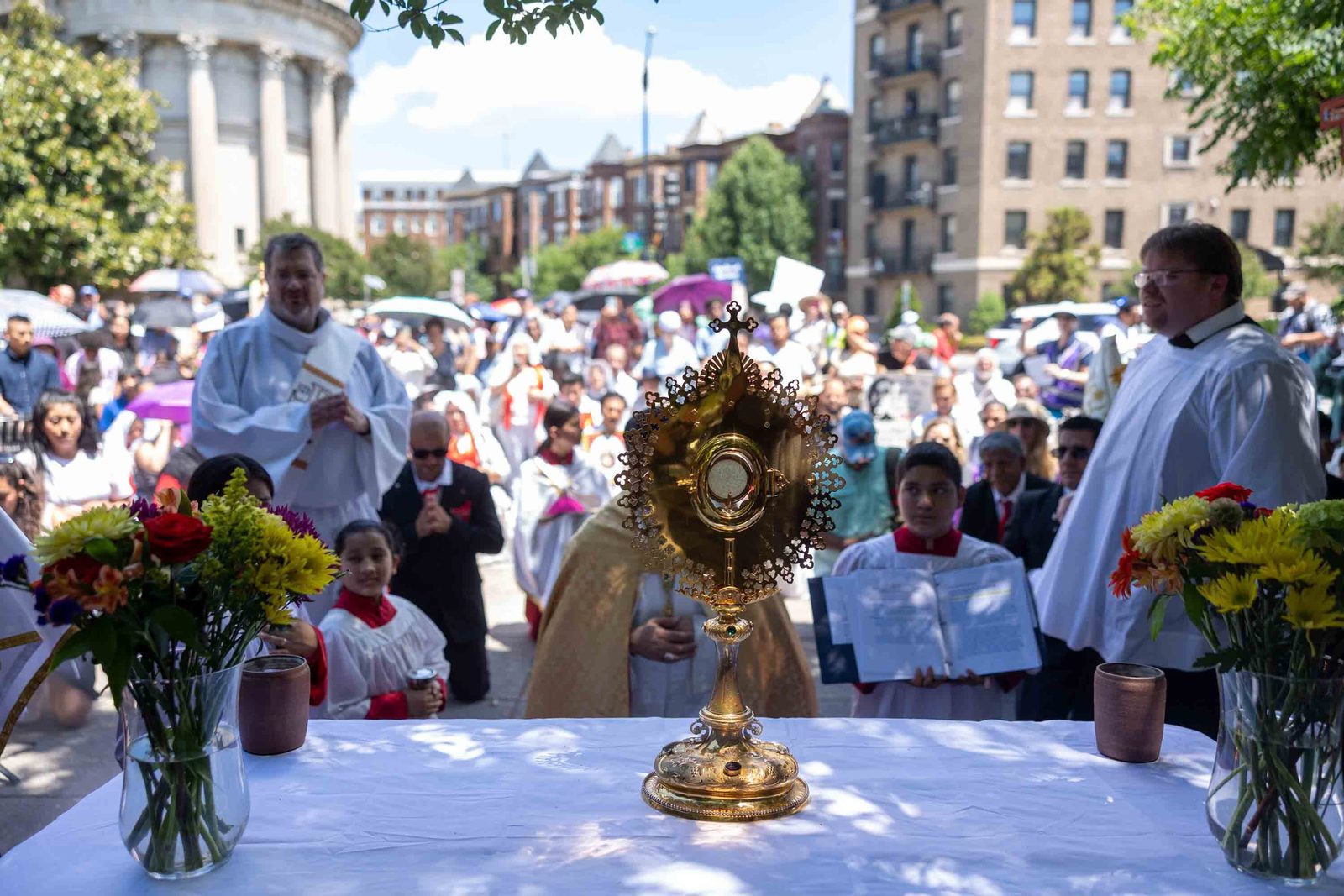 Bishop Evelio Menjívar prays before the Blessed Sacrament at an outdoor altar during the first stop of a Corpus Christi procession held in prayerful solidarity with immigrants and refugees in Washington on June 7, 2026, as hundreds of the faithful gather behind him. (Catholic Standard photo/Mihoko Owada)