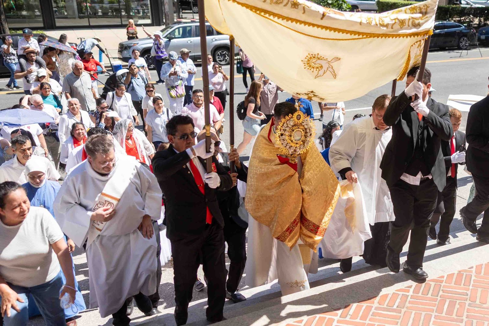 Bishop Evelio Menjívar arrives at the Cathedral of St. Matthew the Apostle carrying the Blessed Sacrament beneath a processional canopy, as hundreds of the faithful follow at the conclusion of a Corpus Christi procession in Washington held in solidarity with immigrants and refugees on June 7, 2026. (Catholic Standard photo/Mihoko Owada)