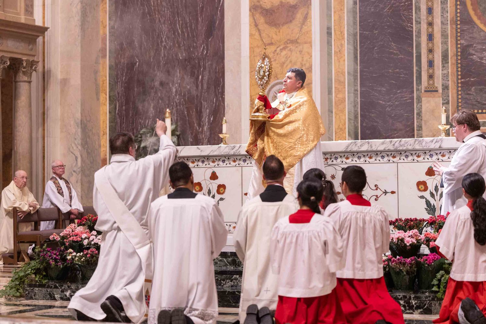 Bishop Evelio Menjívar raises the Blessed Sacrament in a monstrance during Benediction before the kneeling faithful at the Cathedral of St. Matthew the Apostle in Washington at the conclusion of a Corpus Christi procession held in prayerful solidarity with immigrants and refugees on June 7, 2026. (Catholic Standard photo/Mihoko Owada)