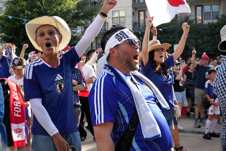 Two Japanese football fans shout joyfully in a crowd on a street.