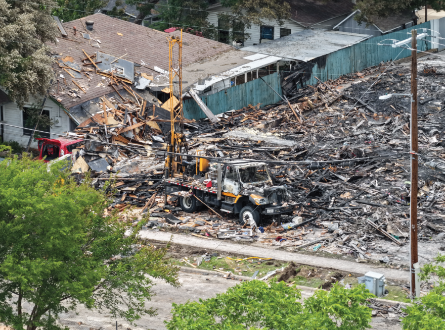 A blackened truck in front of charred rubble from a burnt down apartment complex.
