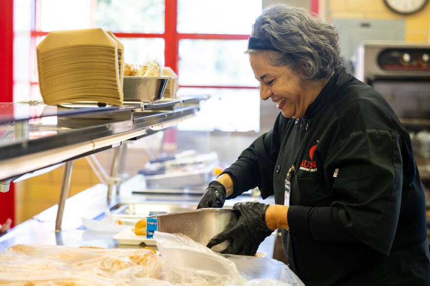 A woman works to prepare lunch inside a school cafeteria.