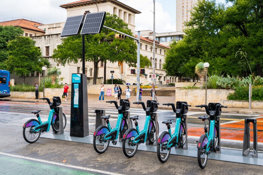 Several Bikeshare bikes are docked at a station on Guadalupe Street in front of the UT Mall. 