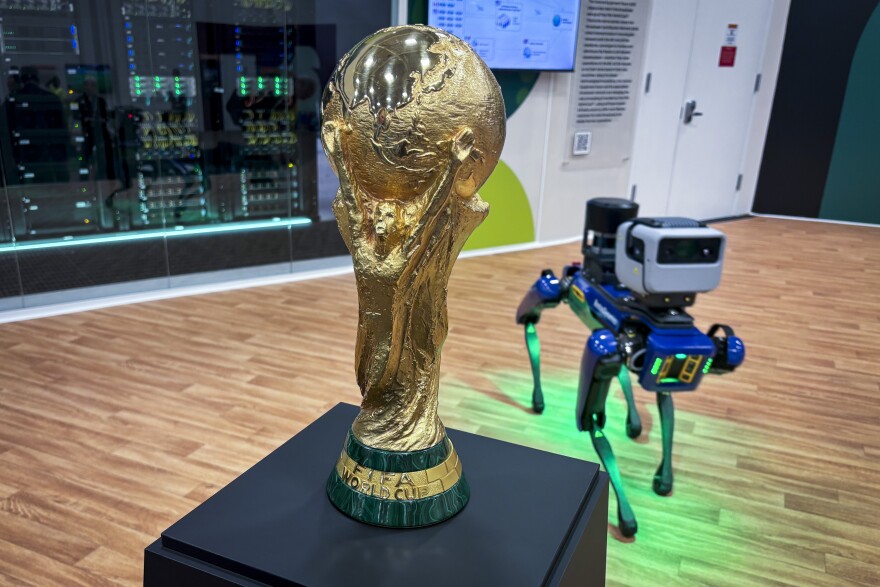 The FIFA World Cup trophy with a BostonDynamics "Spot" robotic dog standing behind it.