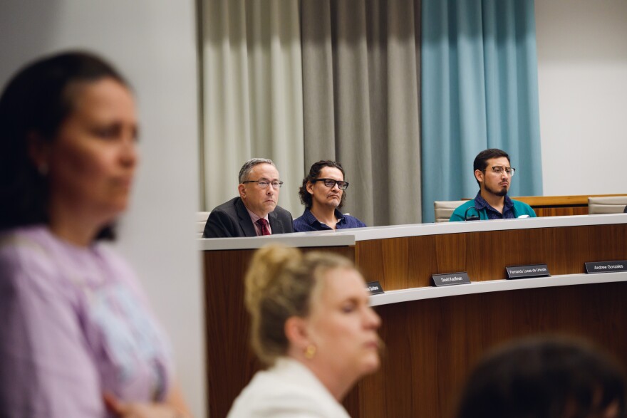 People stand as others sit at a dais in the background.