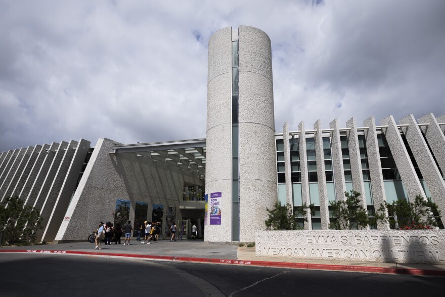 People walk into a building that has vertical slats on the outside and is white.