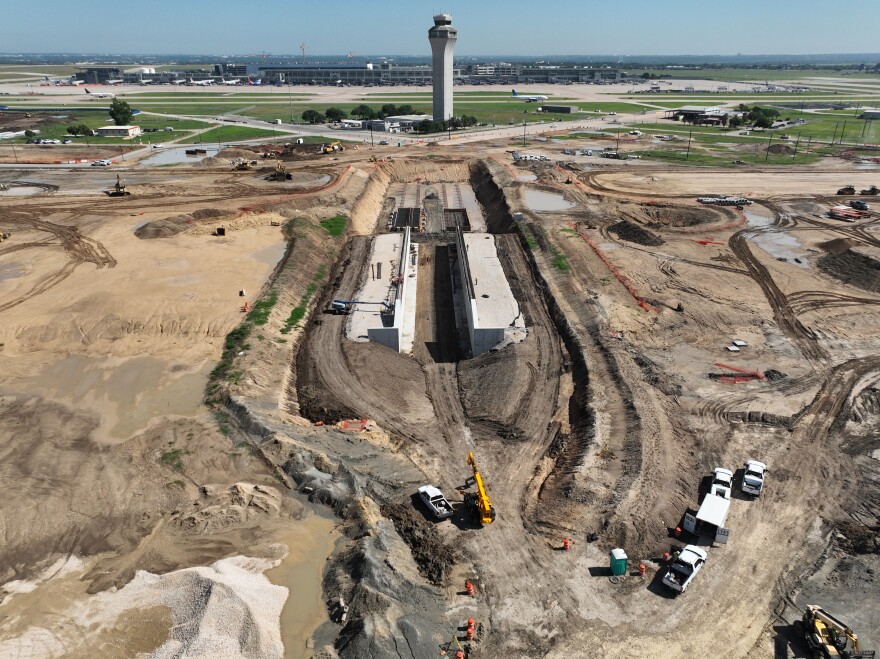 An arial view of construction underway on the ABIA airfield with a large trench being dug. The air traffic control tower is visible in the background.
