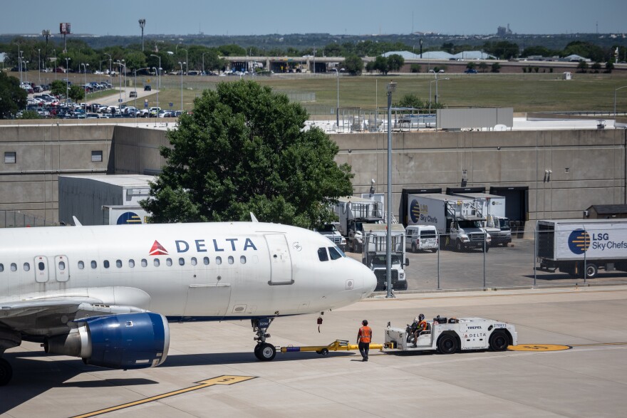 A Delta Airlines airplane parked on the apron in April 2025. Workers are walking around the aircraft.