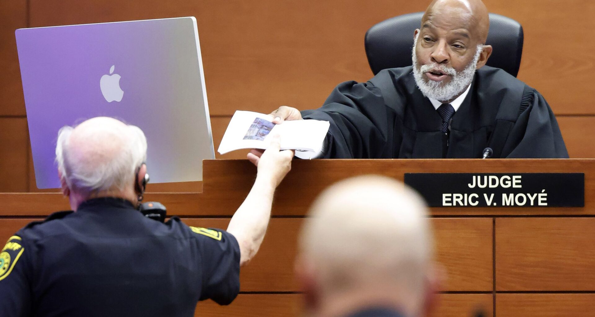 The bailiff hands paperwork to State of Texas Presiding Judge Eric Moyé who later ruled on behalf of three Dallas City Council members who sued the city to delay a vote on the future of City Hall. The judge granted a temporary restraining order to halt a vote by City Council tomorrow. The hearing took place at the George L. Allen, Sr. Courts Building June 9, 2026.