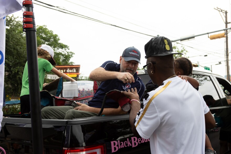 A man in the bed of a pickup truck hands out candy to another man carrying a child.