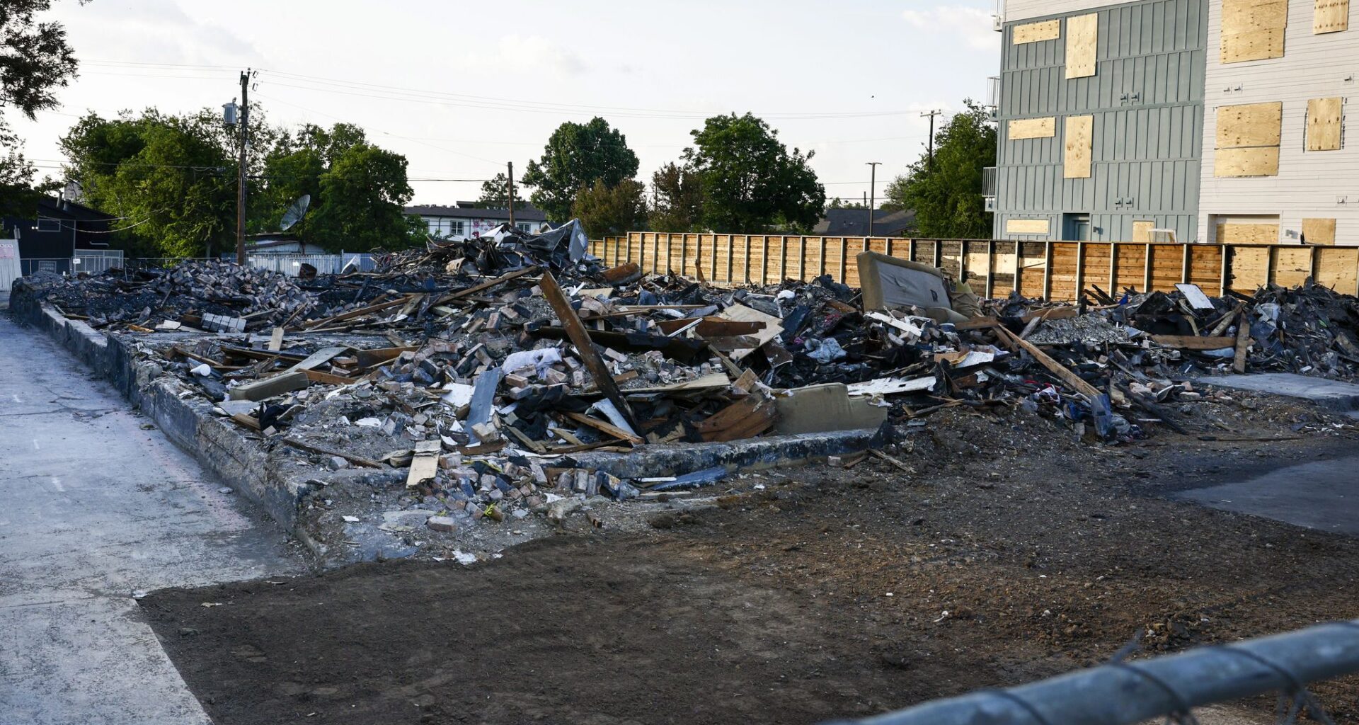 Debris from a deadly explosion and fire at The Clyde apartment building is seen behind a fence in Oak Cliff on Wednesday, June 3, 2026, in Dallas. Three people were killed in the May 28 explosion and fire at the apartment building.