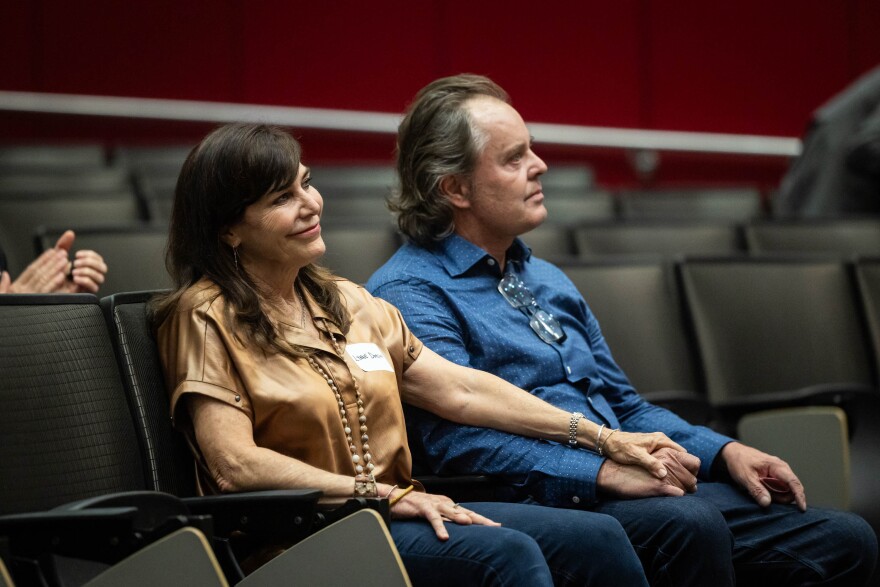 A man and woman sit in seats looking forward.