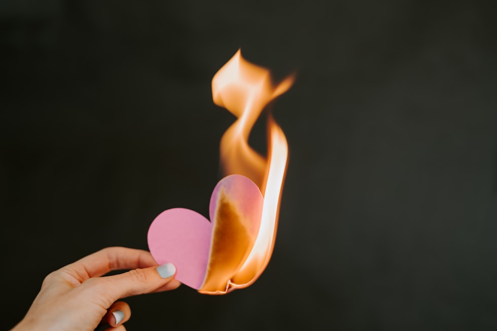 a person holding a paper heart in front of a fire