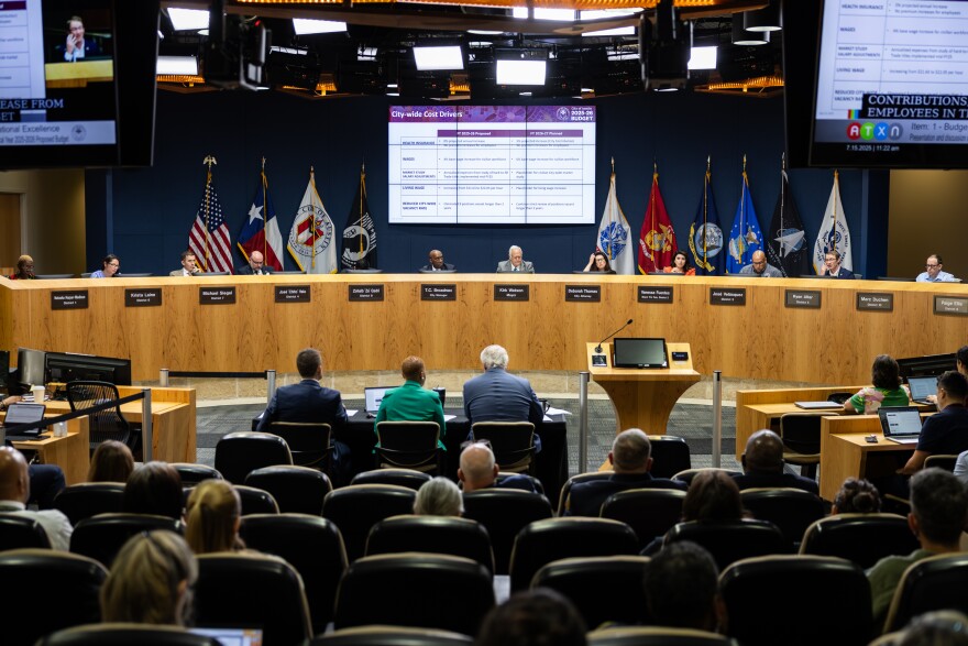 A dais with members of the Austin City Council are seen with an audience in the foreground.