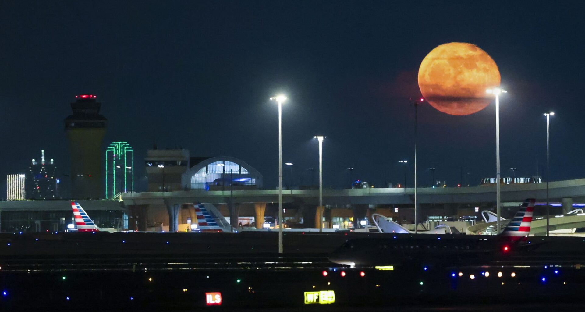 The Blue full moon rises past Dallas Fort Worth International Airport as an American Airlines flight cruises not the run way, on Tuesday, June 2, 2026.