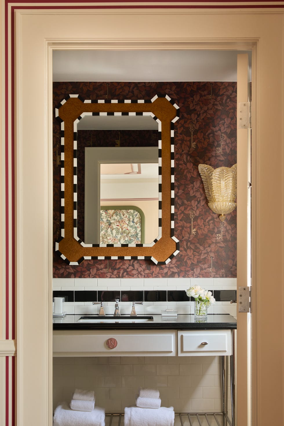 Bathroom with decorative wallpaper, octagonal mirror, and rolled towels.
