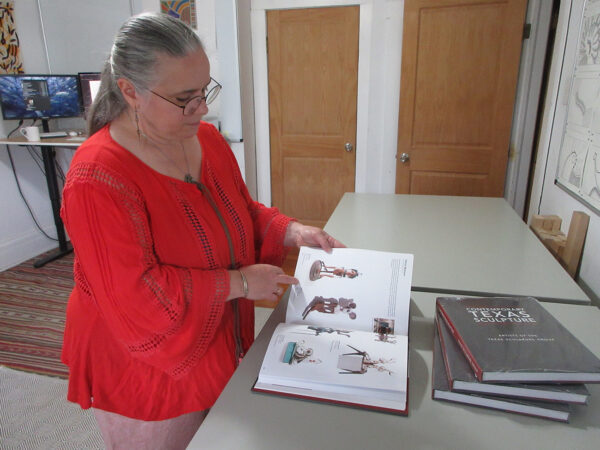 A woman stands at a counter with a book open as she looks at and points to a page.