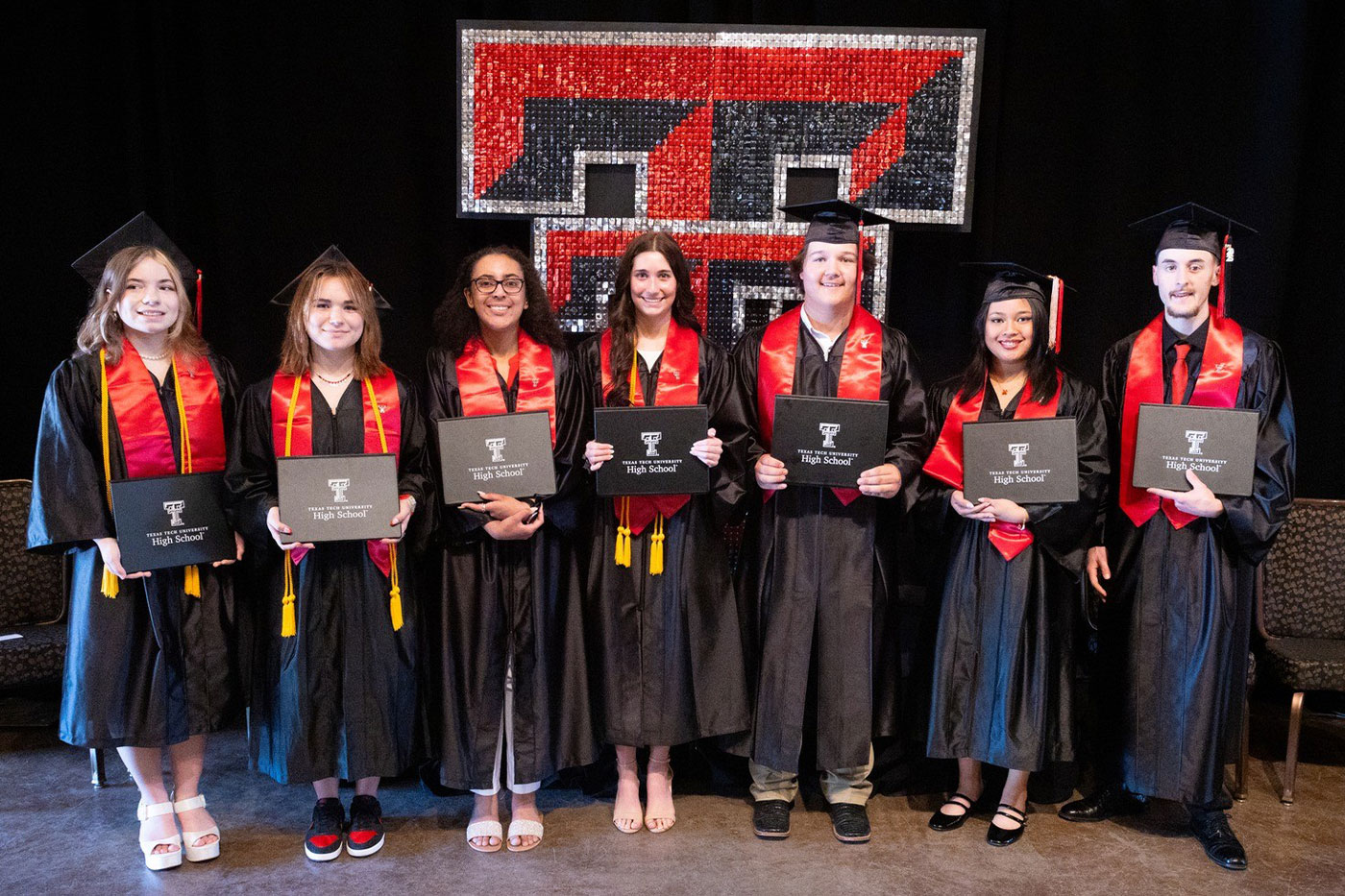Seven Texas Tech K-12 graduates in regalia holding their diplomas