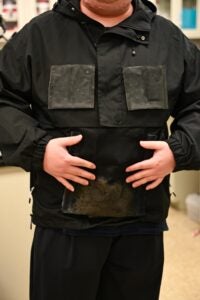 Researcher stands in a lab wearing a black jacket with a water-collecting textile in the front pocket. 