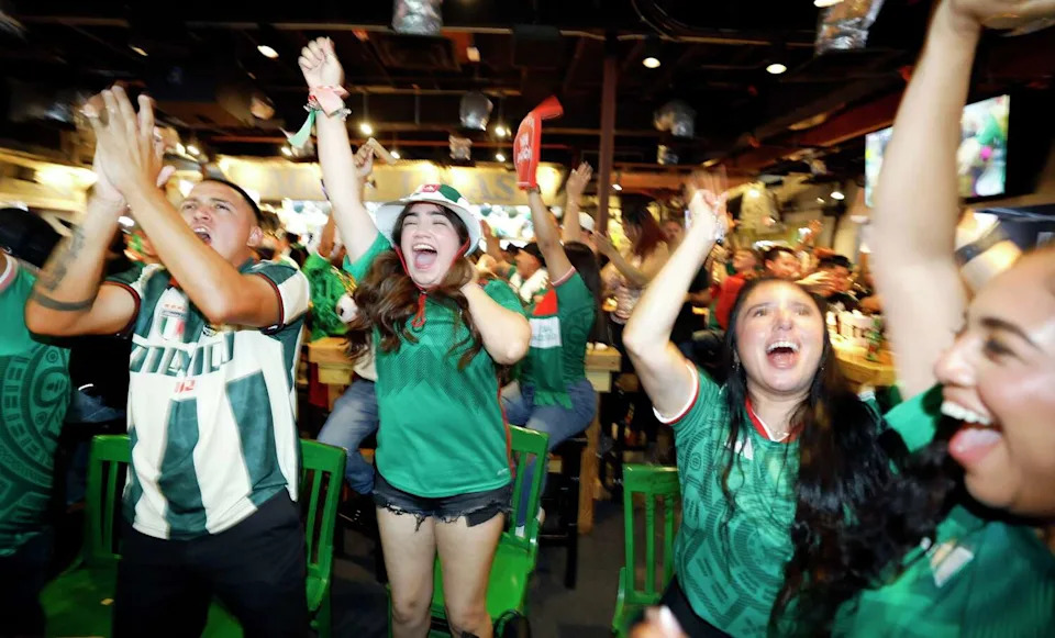 Mexico soccer fans, including Chris Escalera (left) and Johanna Moreno (center) celebrate Julián Quiñones opening goal against South Africa during the opening FIFA World Cup game. The watch party was held at Ojos Locos in Dallas, June 11, 2026. (Tom Fox/The Dallas Morning News)
