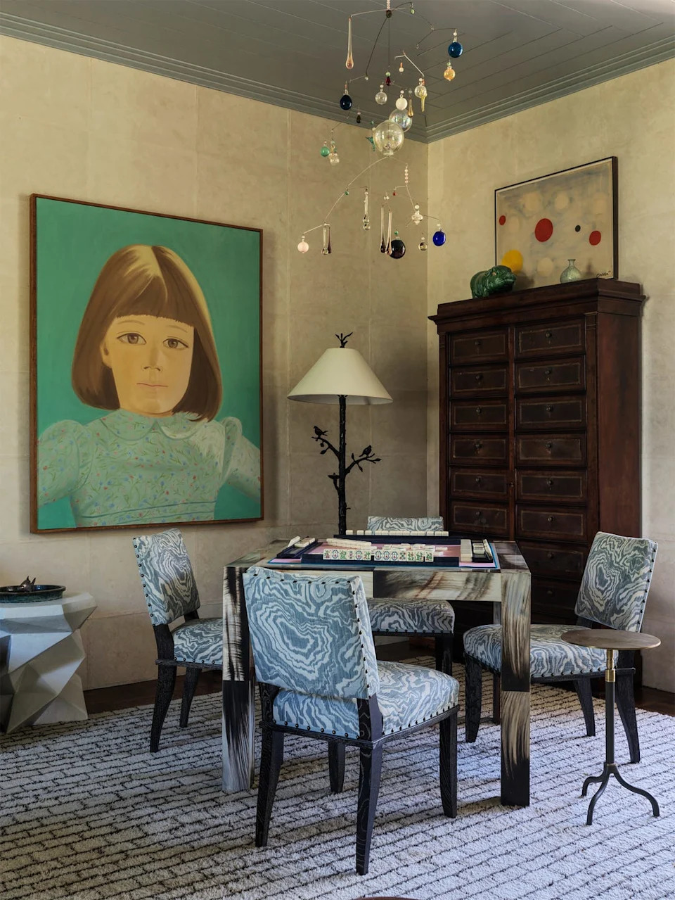 Cozy room with four blue-patterned chairs, a modern table, large child portrait, abstract wall art, and a decorative mobile.