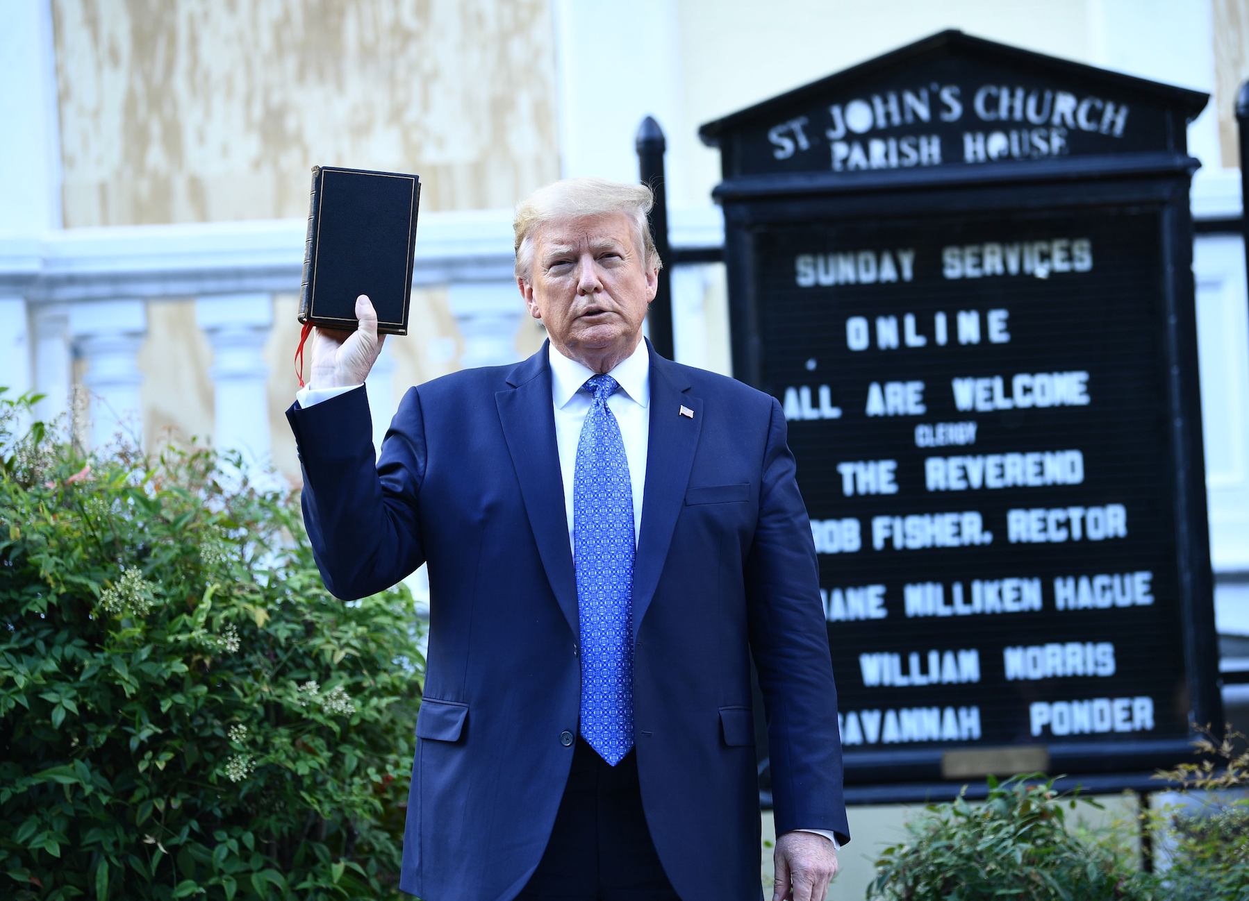 Donald Trump holding a book in front of a church sign listing online Sunday services and clergy names