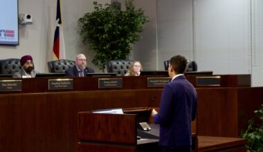 a man speaking to people at a dais