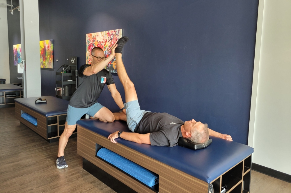 Stretchlab instructor assisting client in stretching their legs while laying down on their back