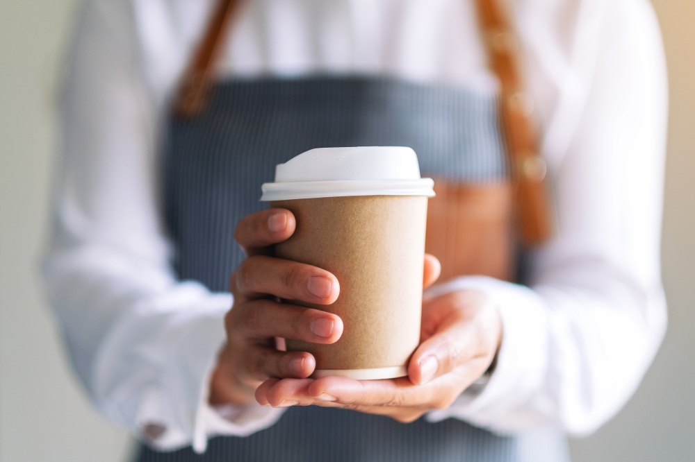 A waiter holding a cup of coffee, the cup has a sleeve around it