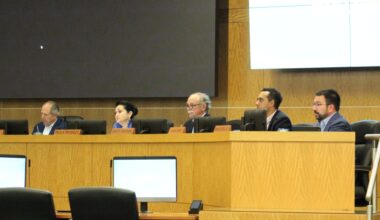 Part of HISD's board of managers sitting behind desks and watching a speaker, who is not pictured