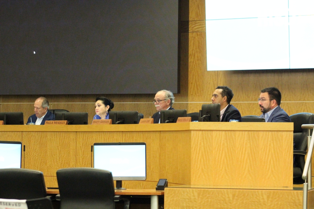 Part of HISD's board of managers sitting behind desks and watching a speaker, who is not pictured