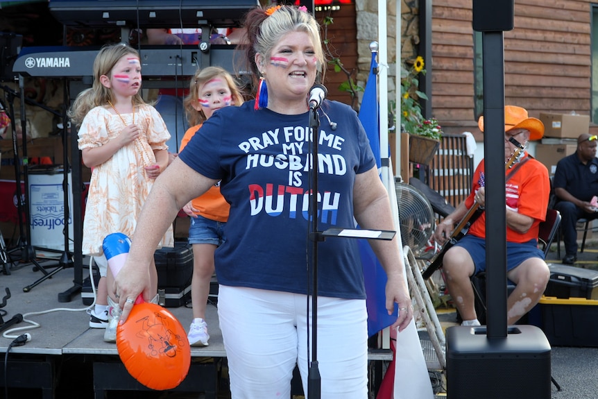 A woman sings into a microphone. She wears a t-shirt saying, "Pray for me, my husband is Dutch".