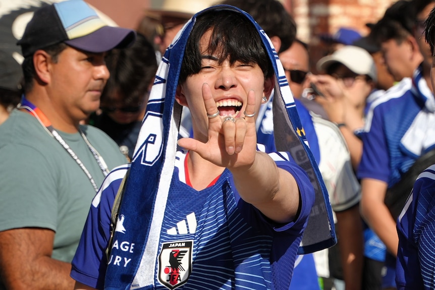 A Japan fan holds out hand in a "rock on" sign and smiles.