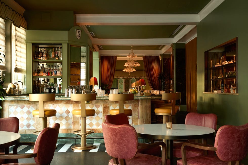Stylish bar interior with green walls, pink chairs, and chandelier.