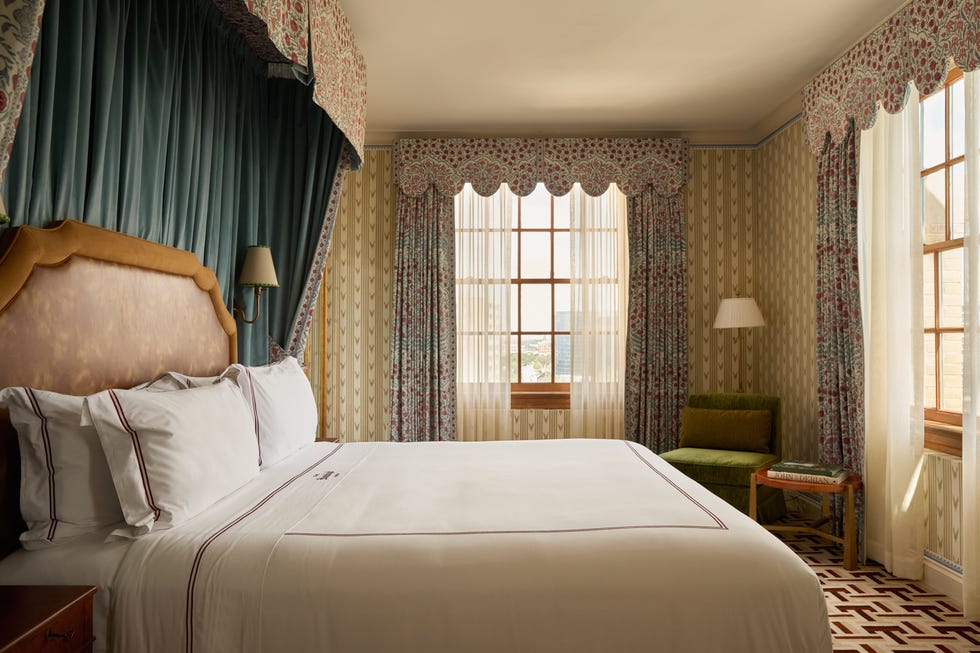 Elegant bedroom with vintage decor, plush bedding, and floral curtains by a sunlit window.