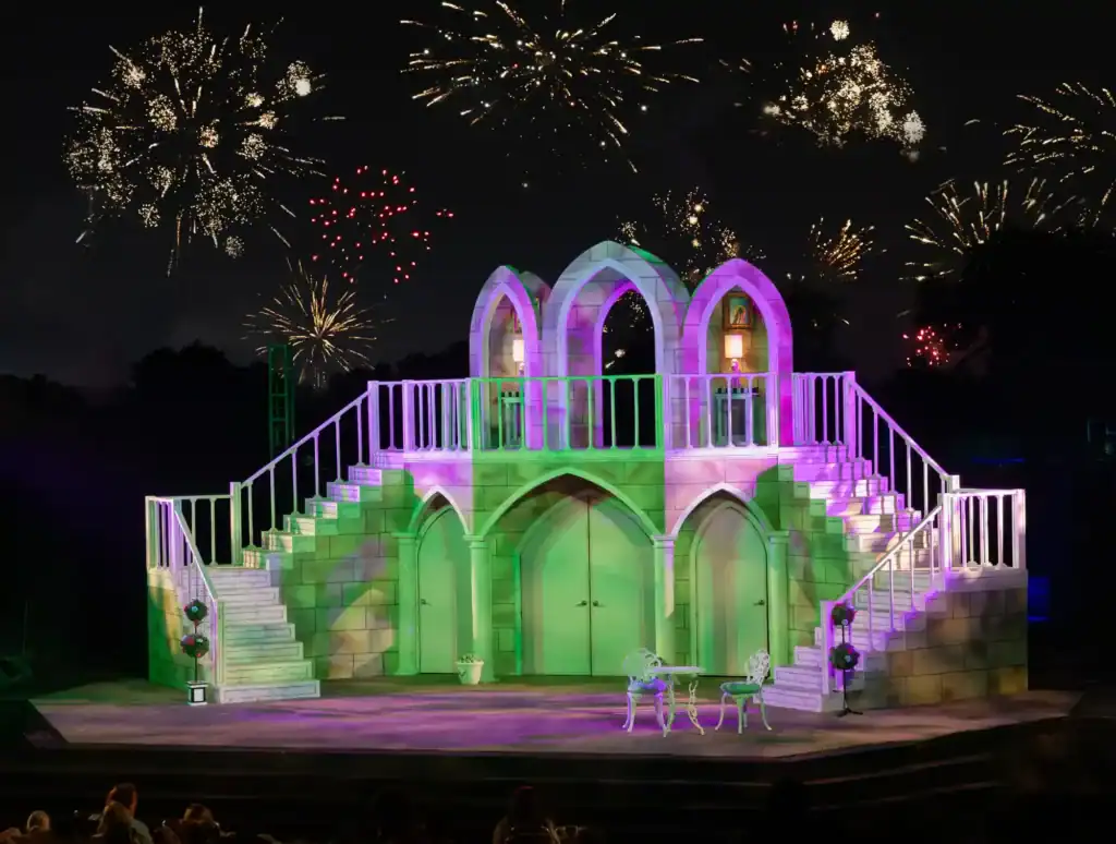 Colorful outdoor theatre stage with fireworks in the night sky.