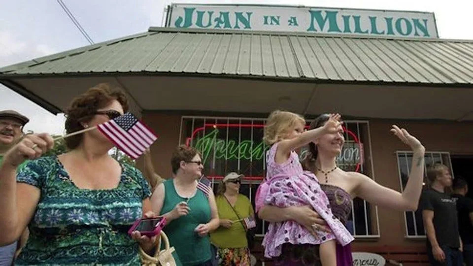 Folks wave at members passing in the 4th of July Barrio Parade as they wait for a table at Juan In A Million in Austin on June 30, 2012. (Austin American-Statesman)