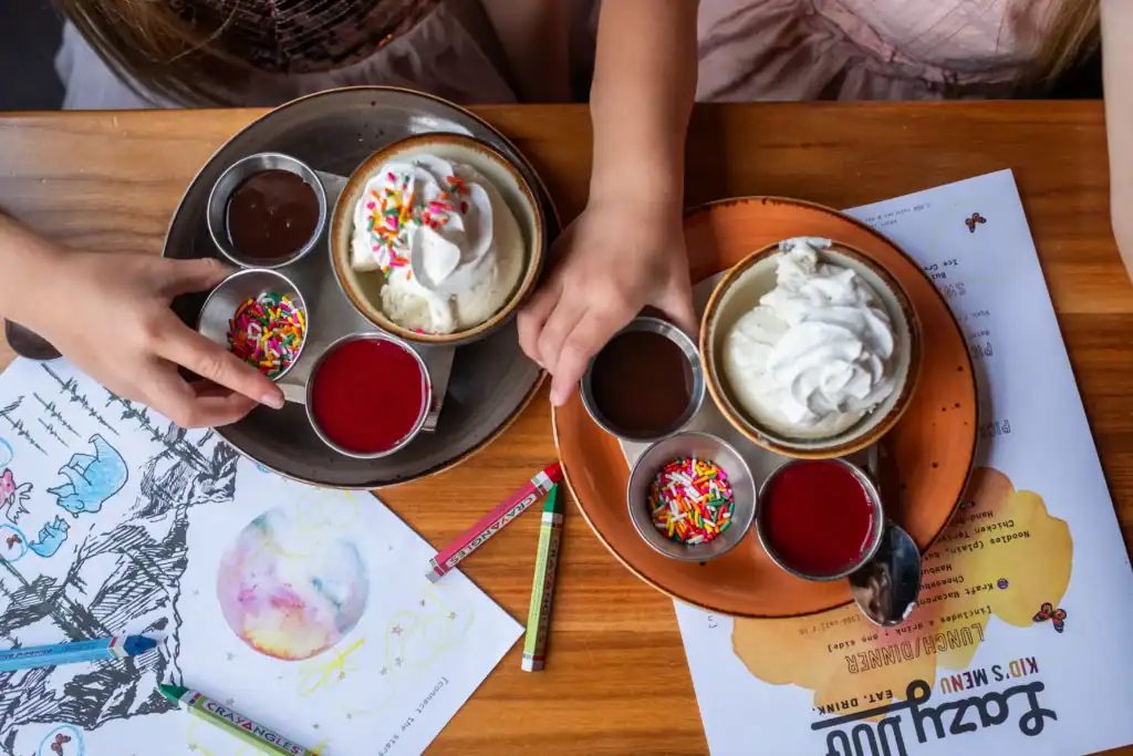 Kids enjoying ice cream with sprinkles and toppings at a restaurant table.