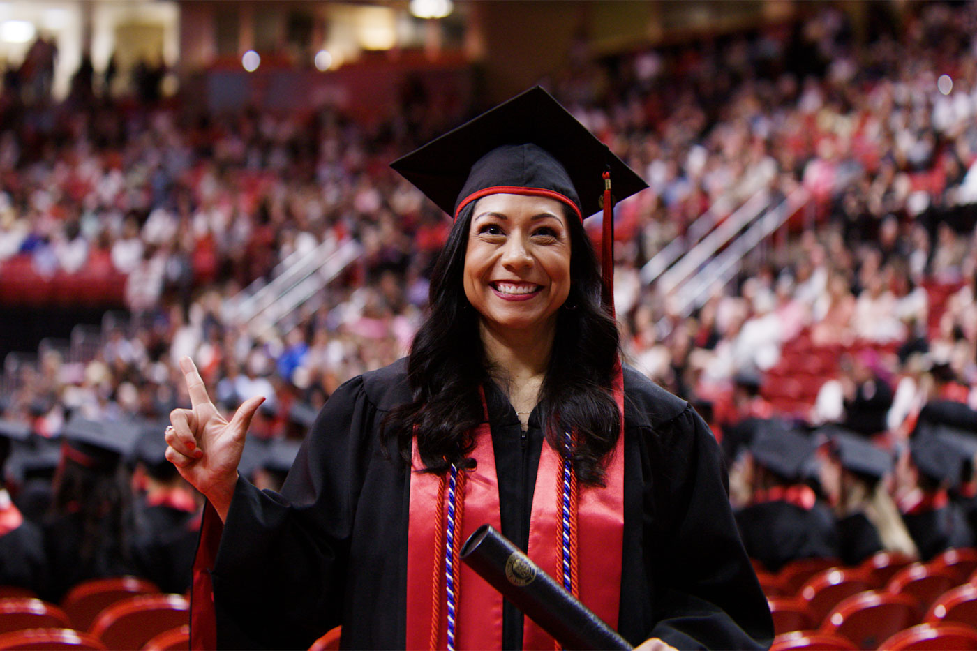 Lesley stands in her regalia in front of a crowd at graduation with her guns up