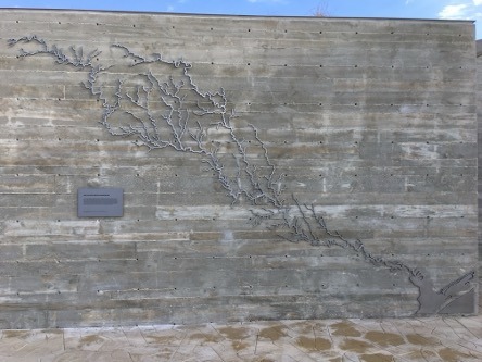 Stone wall with a metal art piece showcasing the San Antonio River Basin